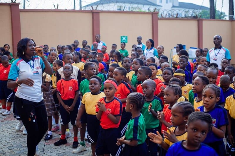 A teacher speaking into a microphone to pupils gathered in the school compound