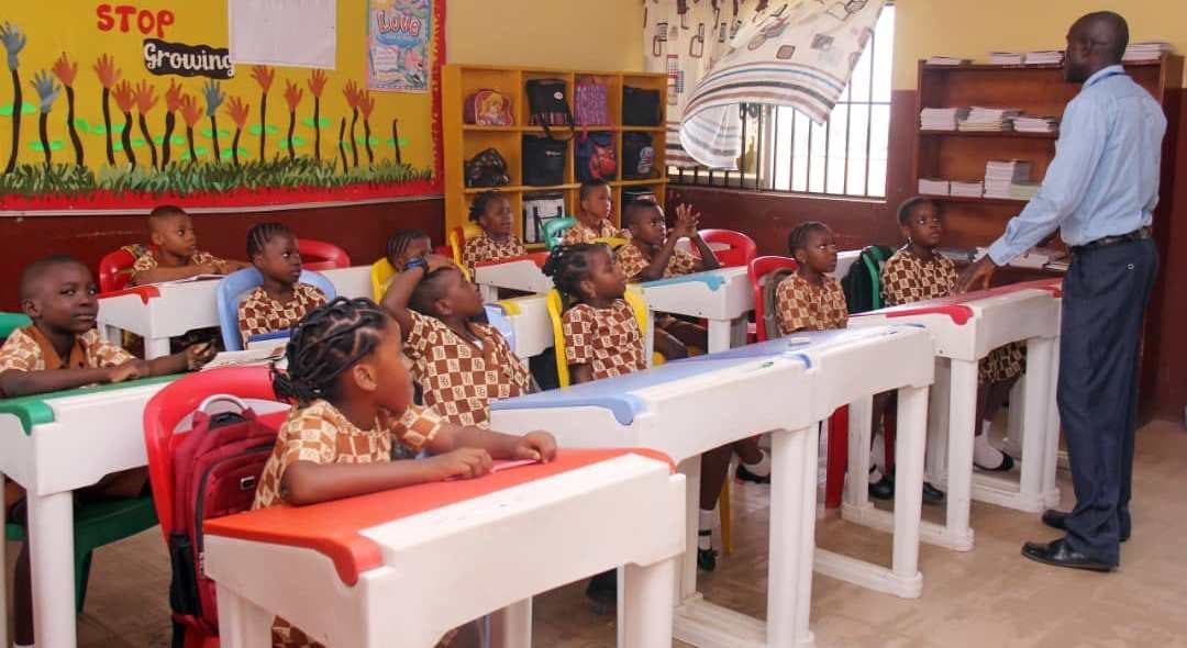 A teacher with pupils seated at their desks in a bright, decorated B and B School classroom