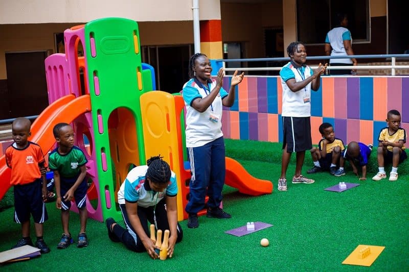 Teachers cheering on young pupils playing beside the slide in the school play area