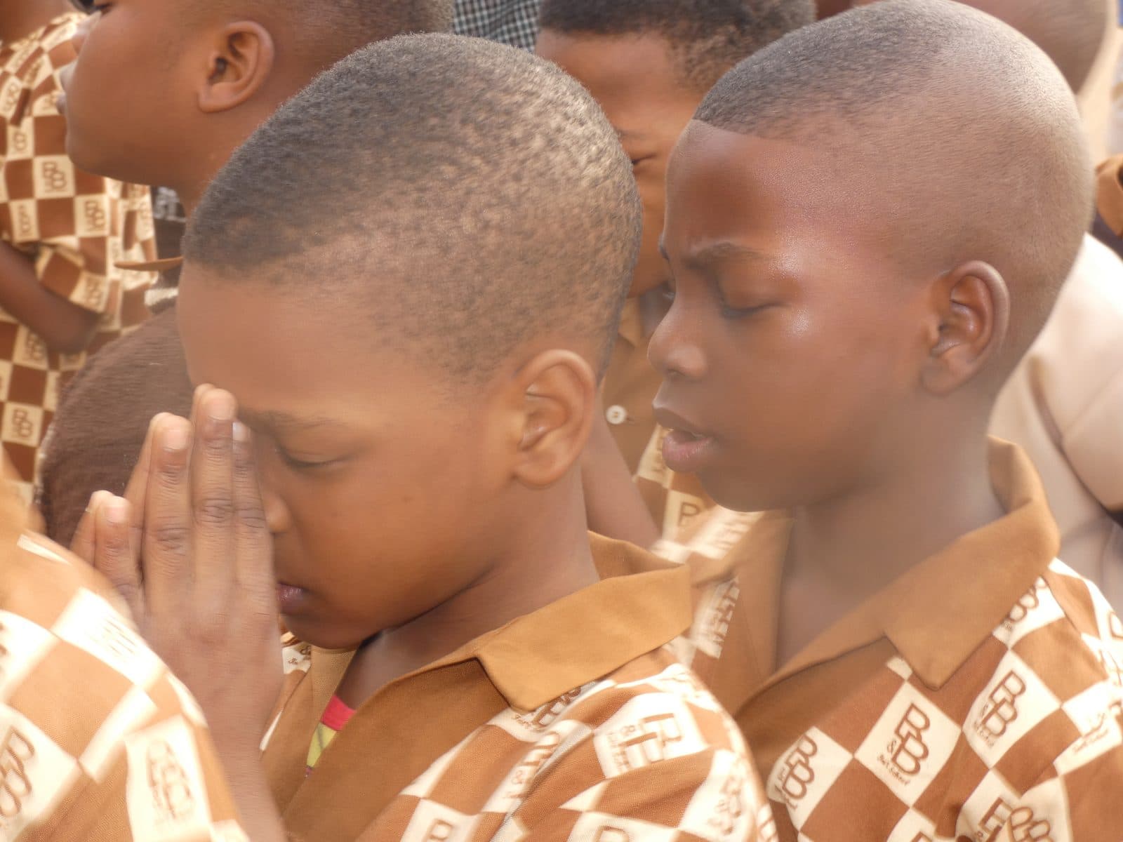 Two B and B School pupils in brown check uniforms with their hands together in prayer