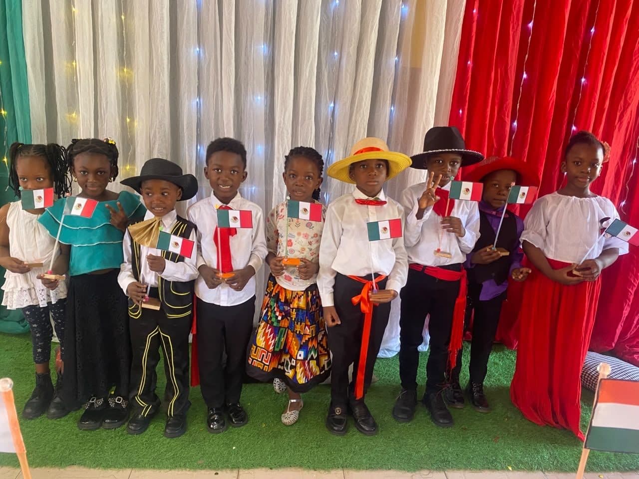 Pupils dressed for Mexico in sombreros, bolero jackets and red sashes, waving Mexican flags on stage