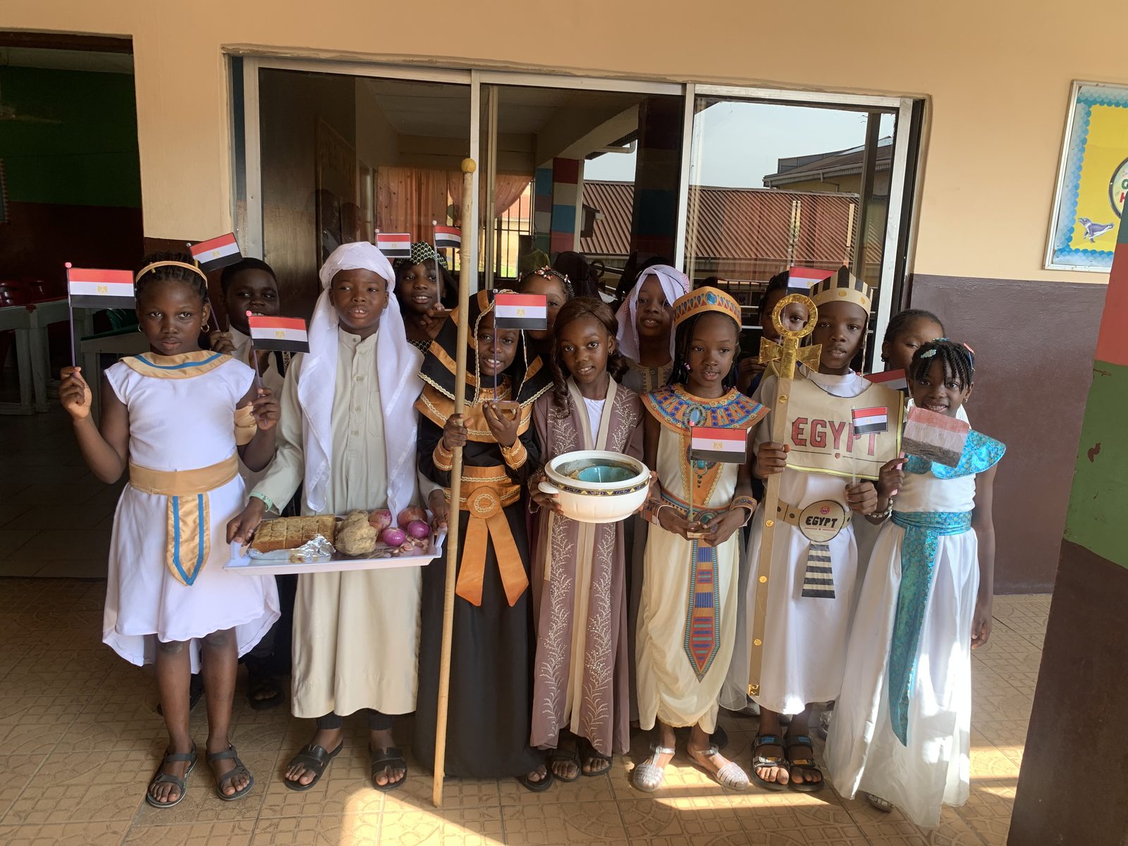 Pupils dressed as ancient Egyptians, with headdresses, a staff and an Egypt sign, waving Egyptian flags