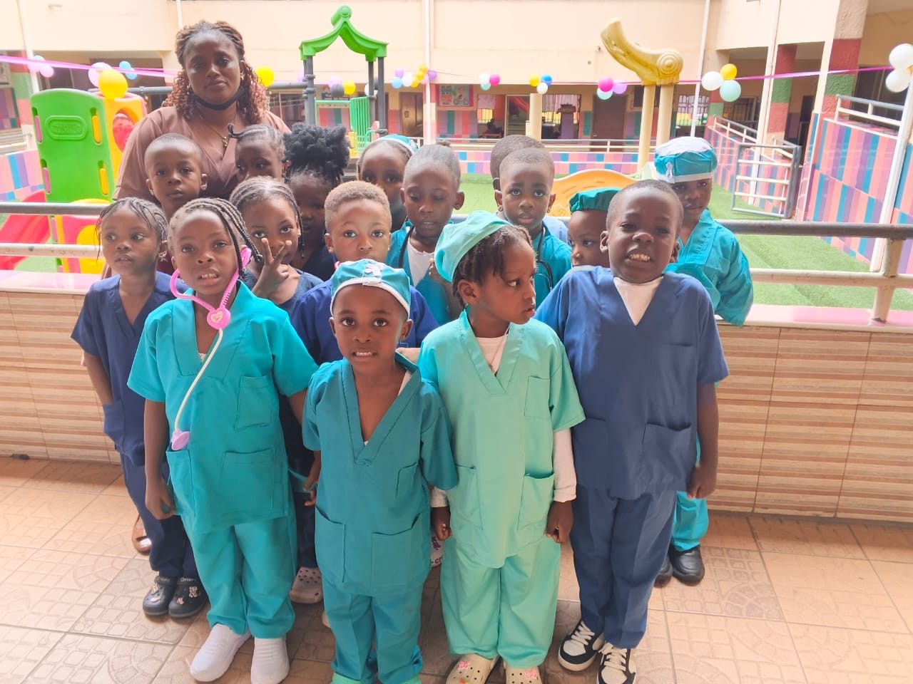 A group of nursery pupils in scrubs and surgical caps on the balcony above the play area